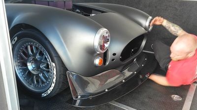 A man in a red shirt is working on a black car