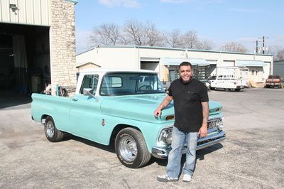 A man is standing next to a blue truck in a parking lot.