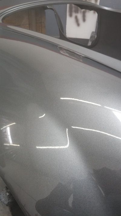 A close up of a silver car with a reflection of a person in the mirror