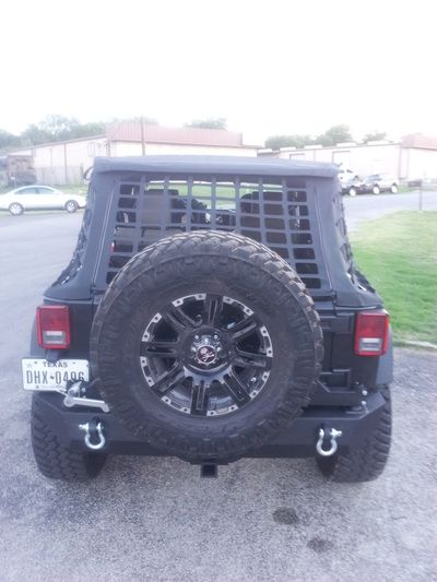 A black jeep with a spare tire is parked in a parking lot