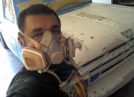 A man wearing a mask is standing in front of a car