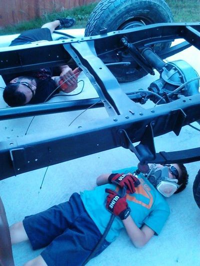 A man wearing a mask is laying under a truck