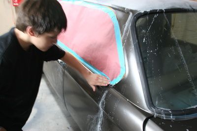 A young boy is cleaning a car with a pink and blue cloth