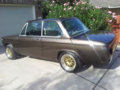 A brown car with gold wheels is parked in a driveway