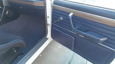 The inside of a white car with the door open and a black seat