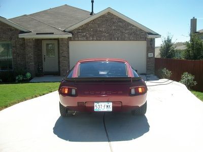 A red porsche is parked in front of a brick house