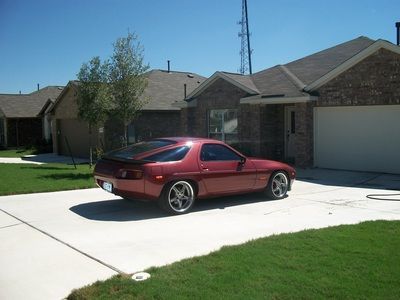 A red sports car is parked in a driveway in front of a brick house