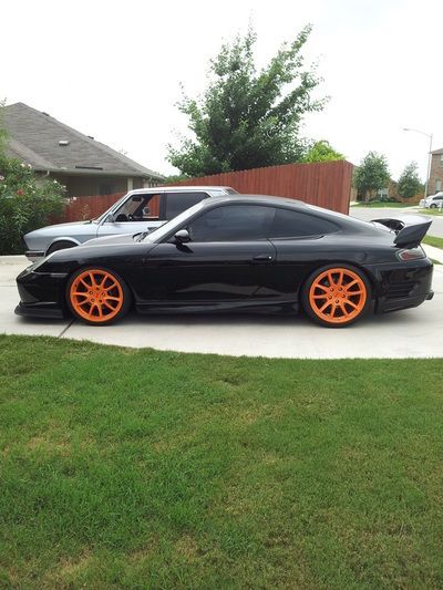A black car with orange wheels is parked in a drivewa