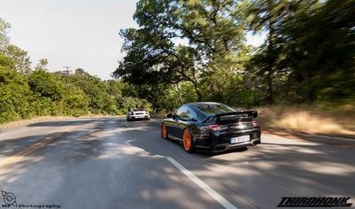 A black sports car is driving down a road next to trees