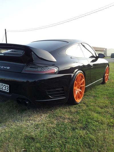 A black car with orange wheels is parked in a grassy field