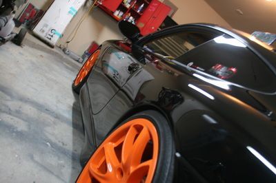 A black car with orange wheels is parked in a garage