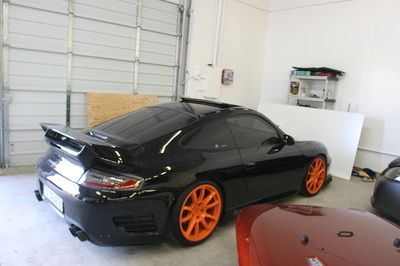 A black car with orange wheels is parked in a garage