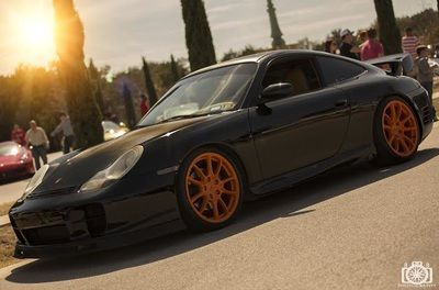 A black porsche 911 with orange wheels is parked on the side of the road