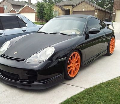 A black sports car with orange wheels is parked in a driveway