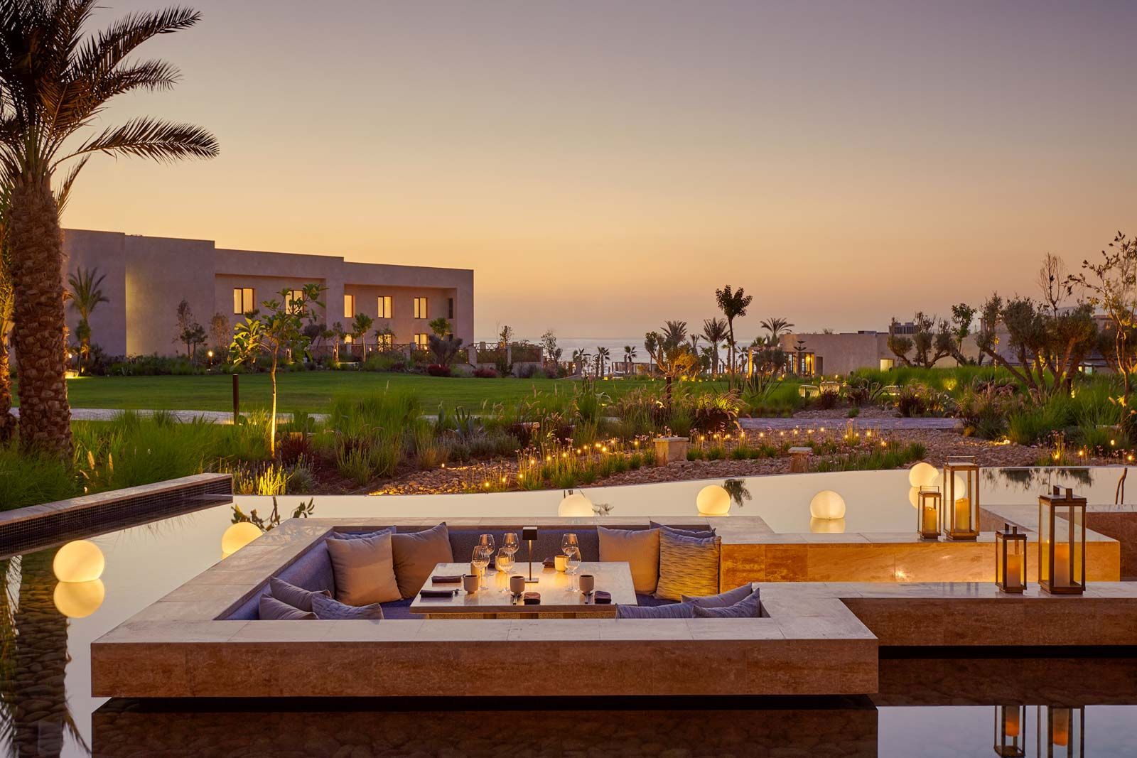 A patio area with a couch and a table next to a pool at sunset.