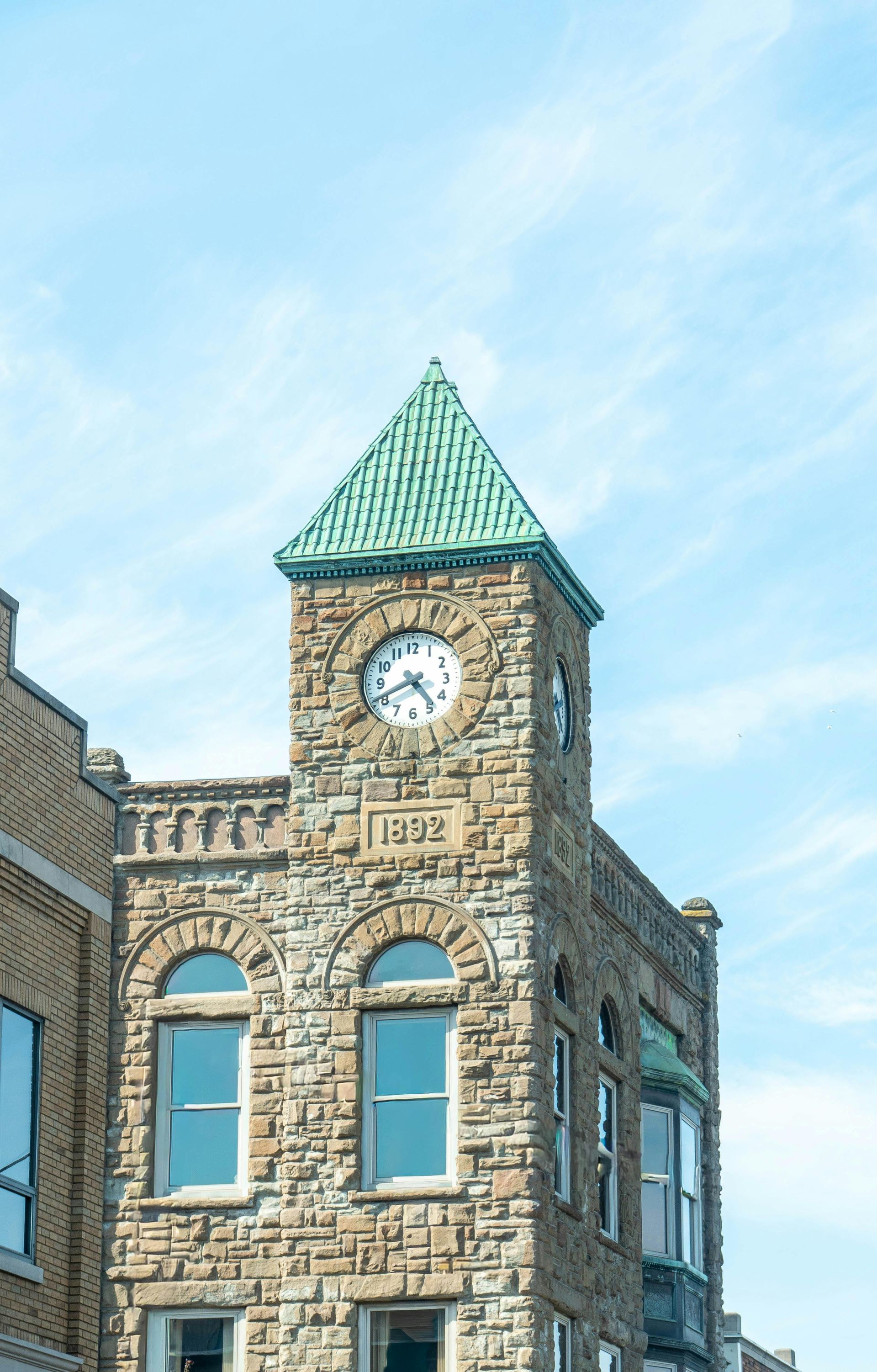 Stone clock tower with green roof against a blue sky.
