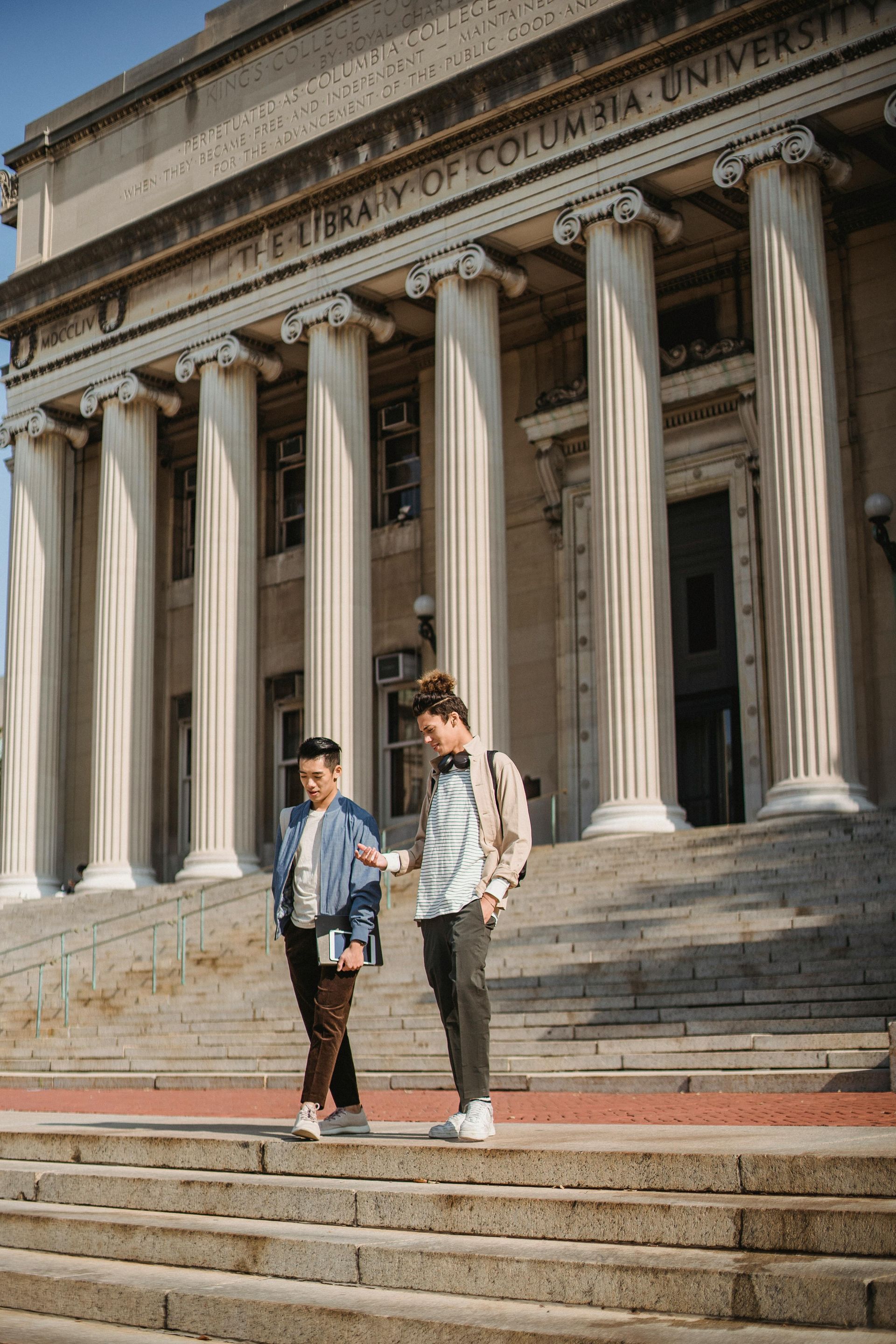 Two people on steps of Columbia University library. One points; the other looks at a phone.