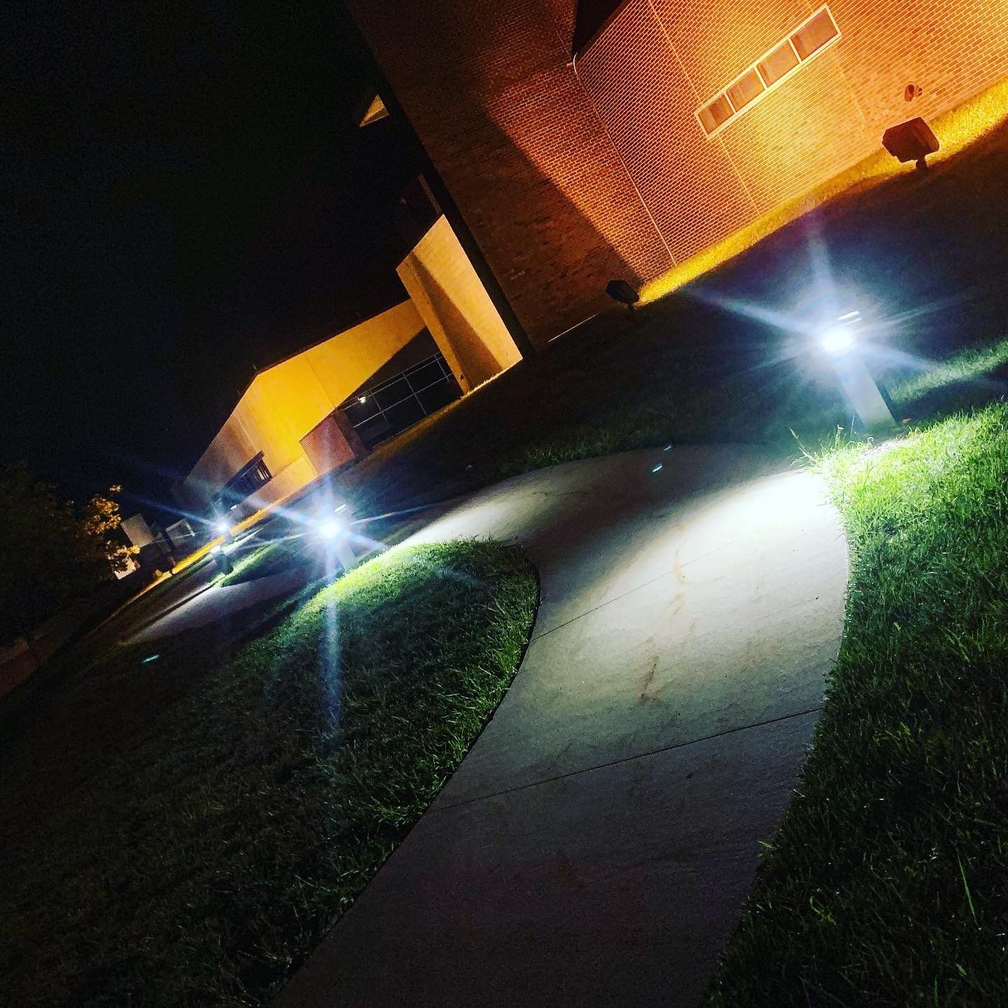 A sidewalk is lit up at night in front of a brick building