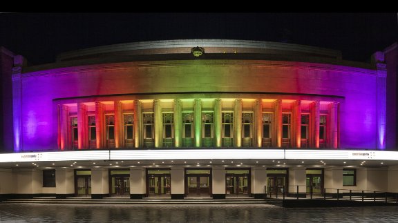 A large building is lit up with rainbow lights at night.