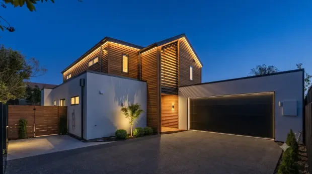 Modern two-story house at dusk with warm exterior lighting and a double garage
