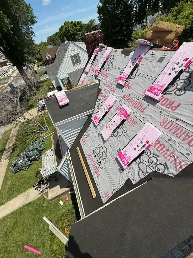 Roof under repair with pink underlayment sheets and shingles, viewed from above on a sunny day