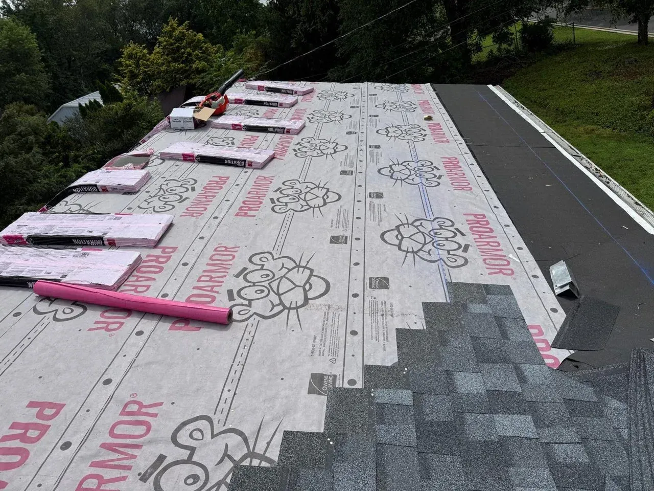 Roof underlayment being installed, with pink insulation boards and shingles on a sloped roof