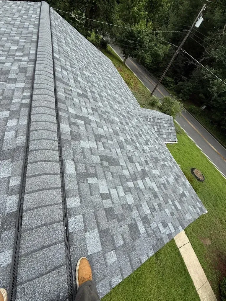 Roofing shingles on a steep gray roof, viewed from above beside a grassy yard and road.