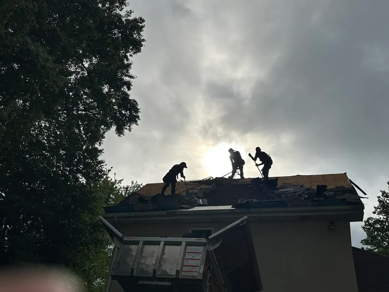 Workers on a roof silhouetted against a cloudy sky, likely doing repairs or construction