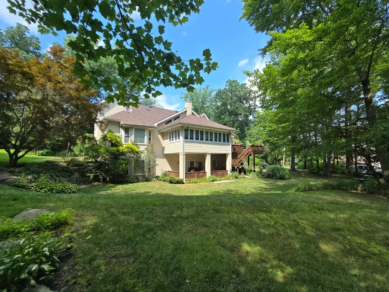 Large beige house with a screened porch, surrounded by a green lawn and leafy trees under a blue sky