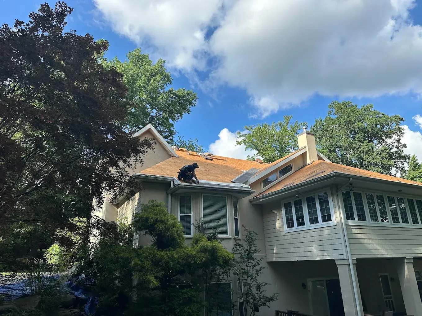 House with white stucco walls, terracotta roof, and screened porch under trees and a blue sky with clouds