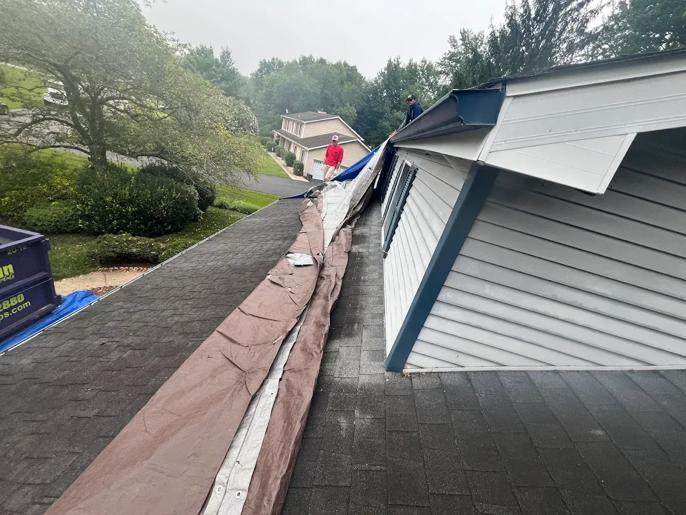 Roof damage along a sloped roof with a torn ridge and a person inspecting in the distance