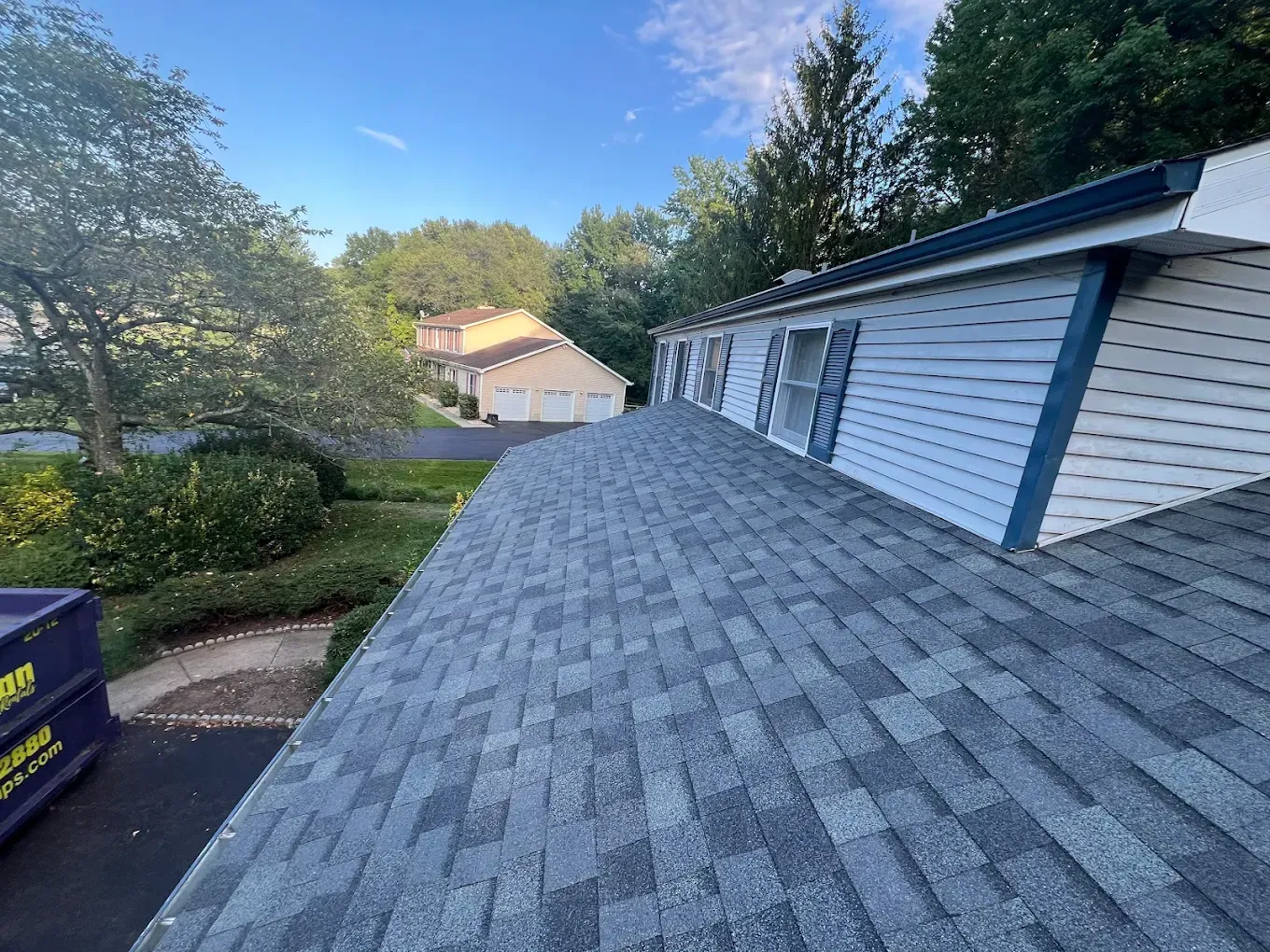 Roof shingles and house siding viewed from above, with trees and a driveway in the background