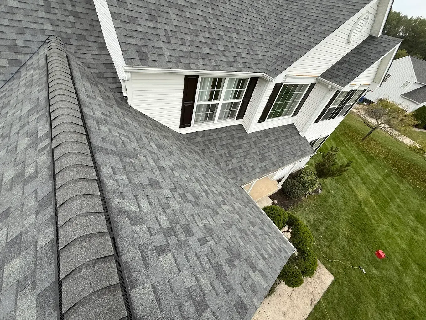 Aerial view of a gray shingled roof beside white siding and a green lawn.
