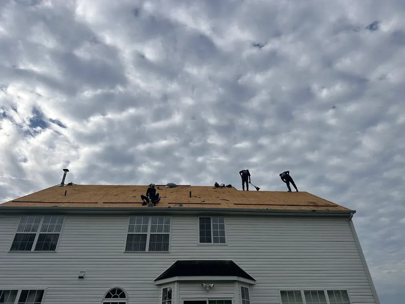 Workers on a house roof repairing shingles under a cloudy sky