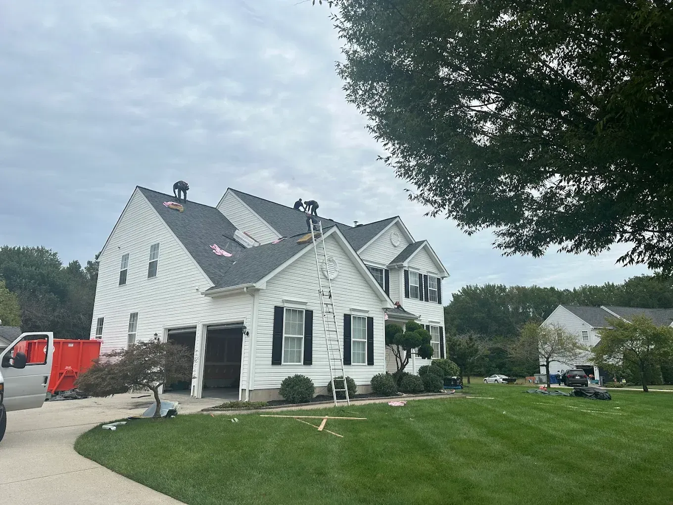 White house with black shutters and a green lawn under a cloudy sky, with a red truck nearby