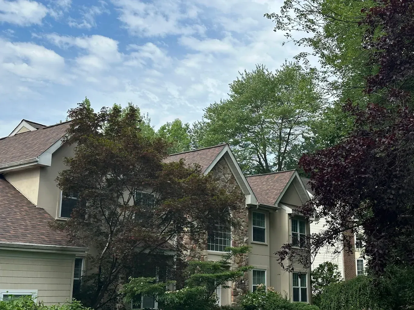 Suburban townhouse with beige siding and green trees under a partly cloudy sky