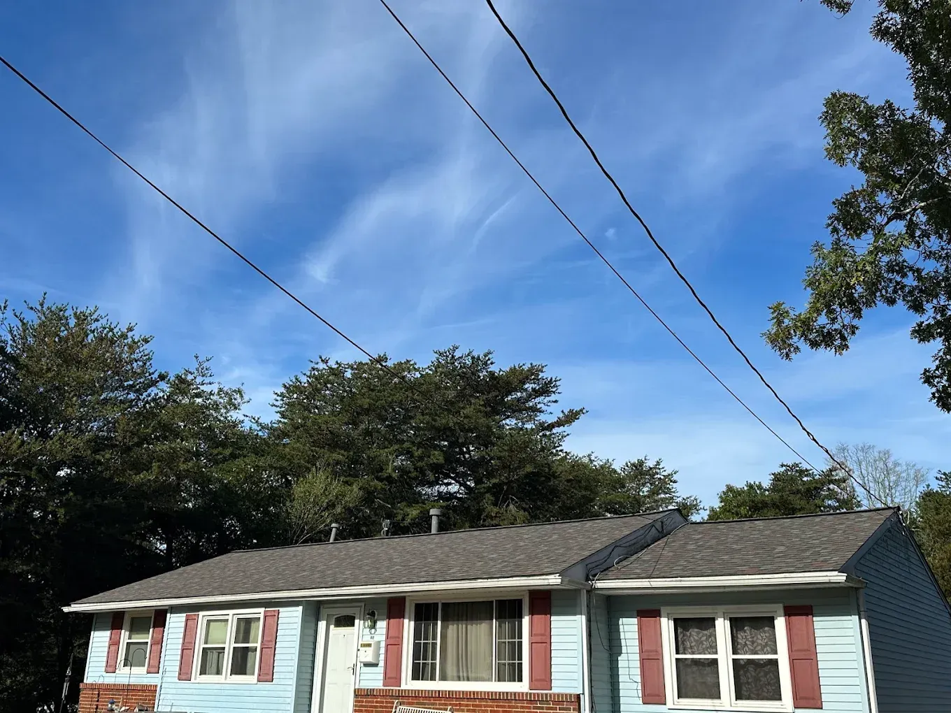 Single-story blue house with white trim under a blue sky, framed by trees and power lines.