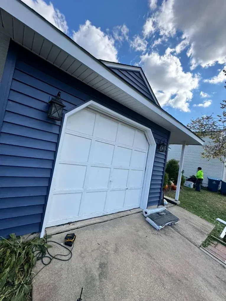Blue house garage with white door, driveway, and a worker in a neon vest near the yard.