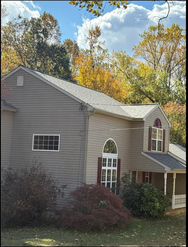 Suburban two-story gray house with white trim, autumn trees, and a small front porch