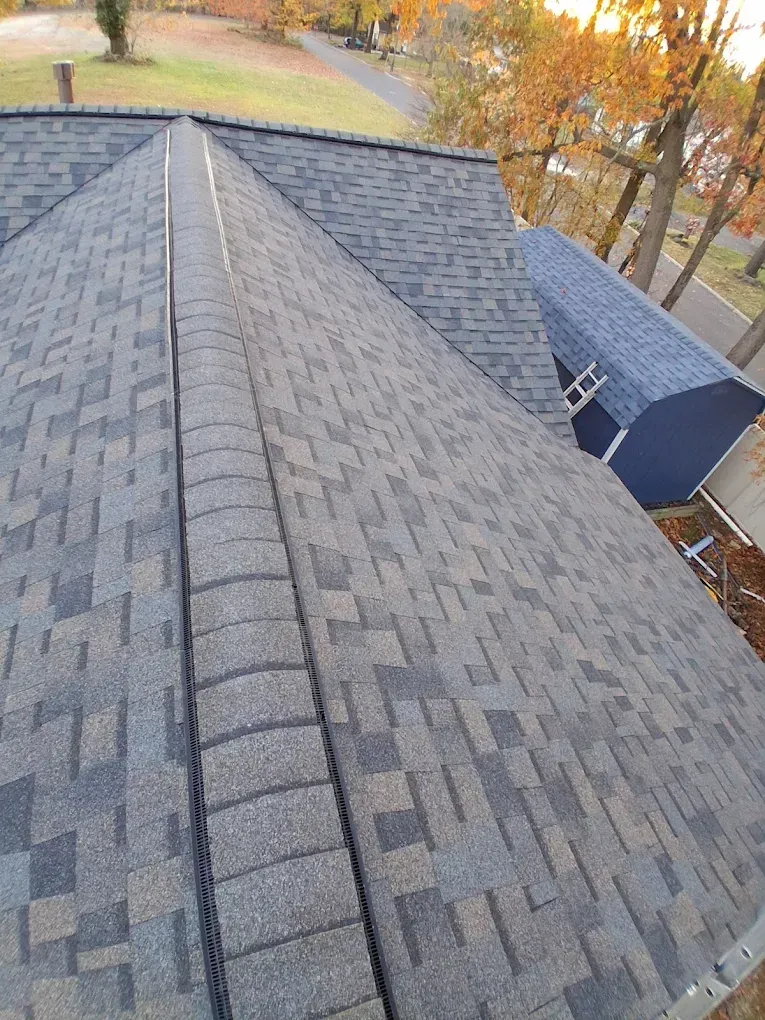View from a roof ridge with gray shingles and autumn trees in the background