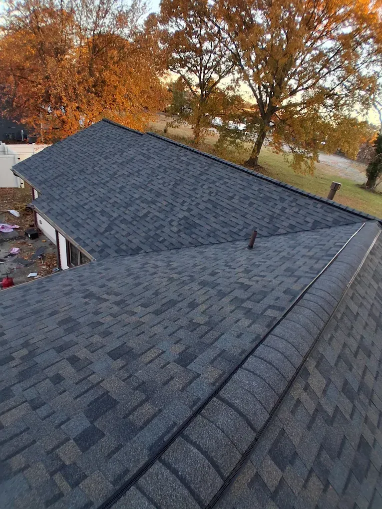 Rooftop with gray shingles, autumn trees in the background, viewed from above.