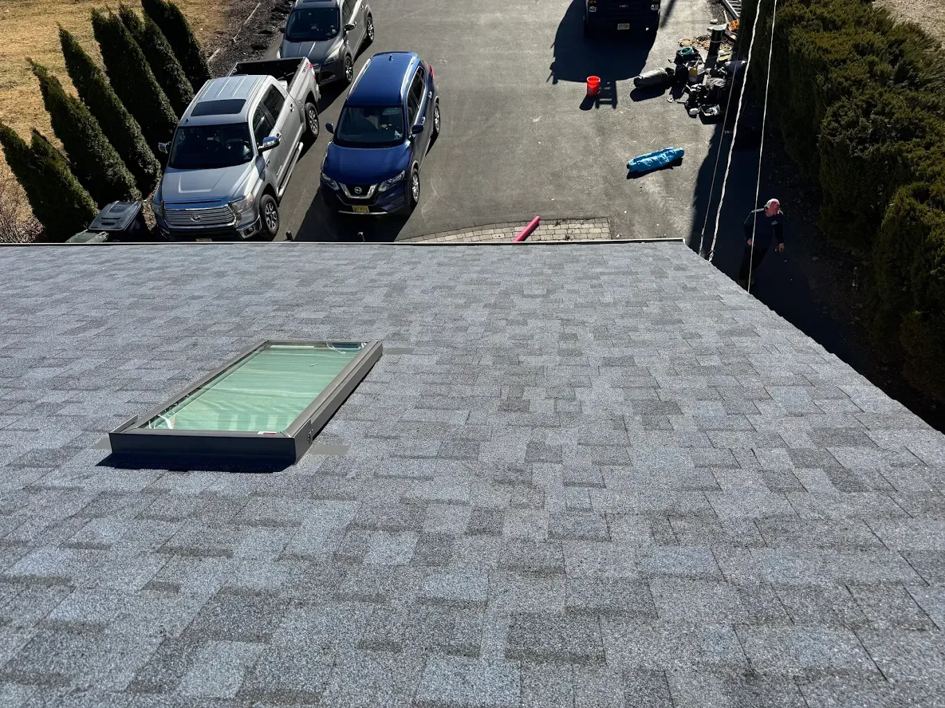 View from a rooftop with a skylight, overlooking parked cars and a residential driveway below.