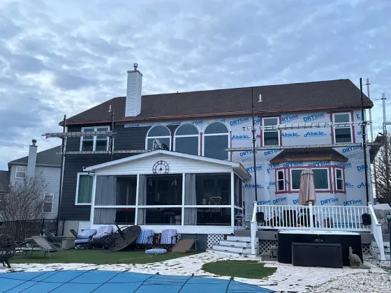Snowy two-story house with a white porch and arched windows under a cloudy sky