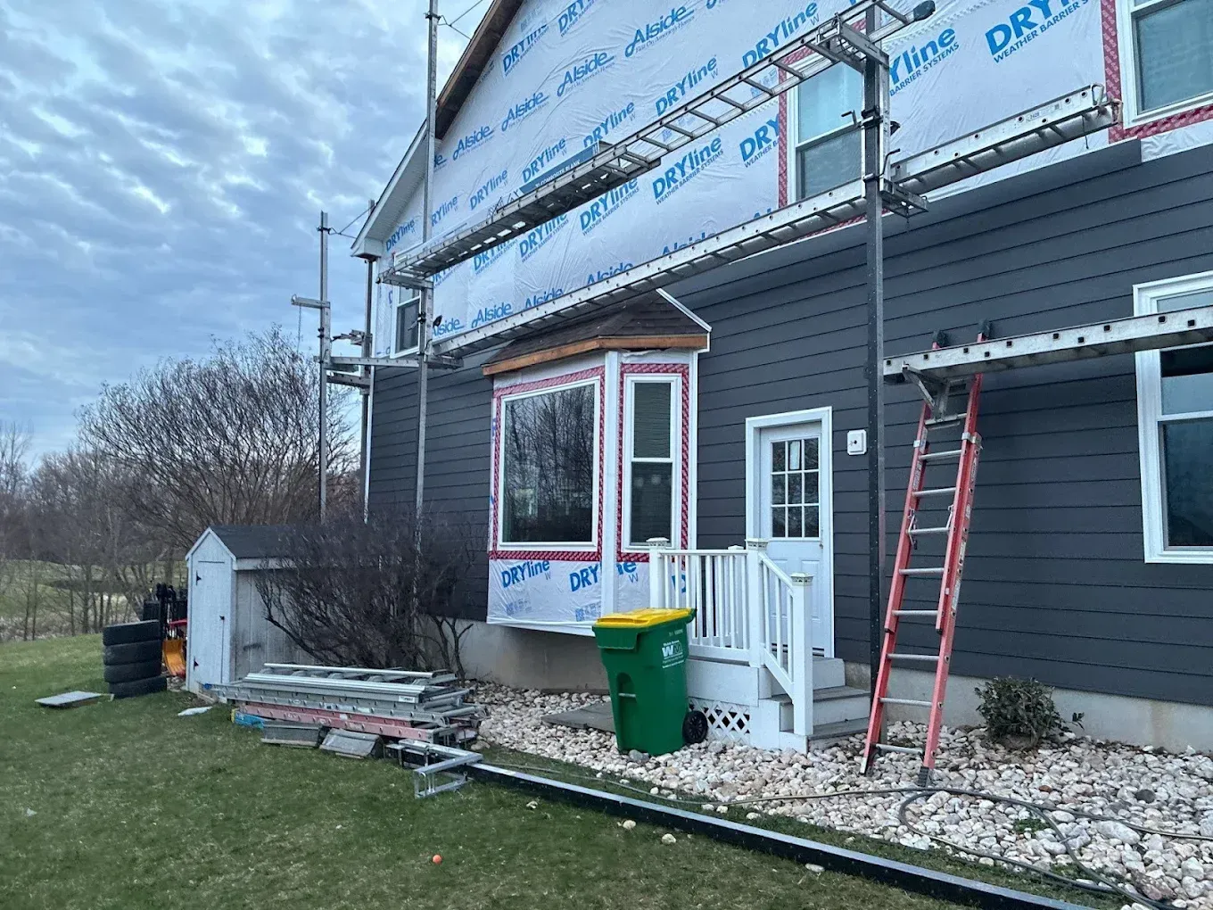 House exterior under renovation with scaffolding, ladder, and construction materials along the side wall