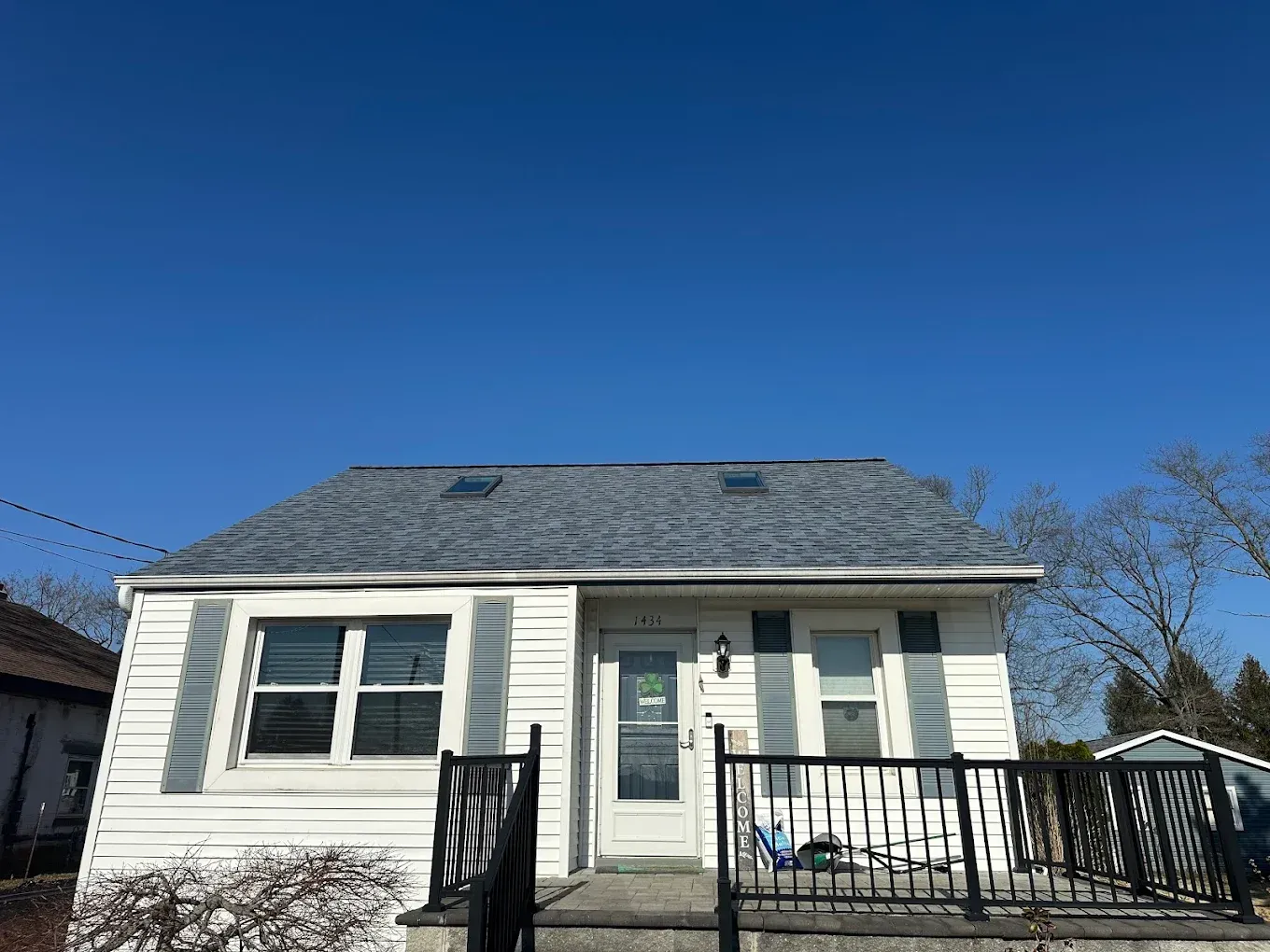 Small white house with gray roof and front porch under a clear blue sky