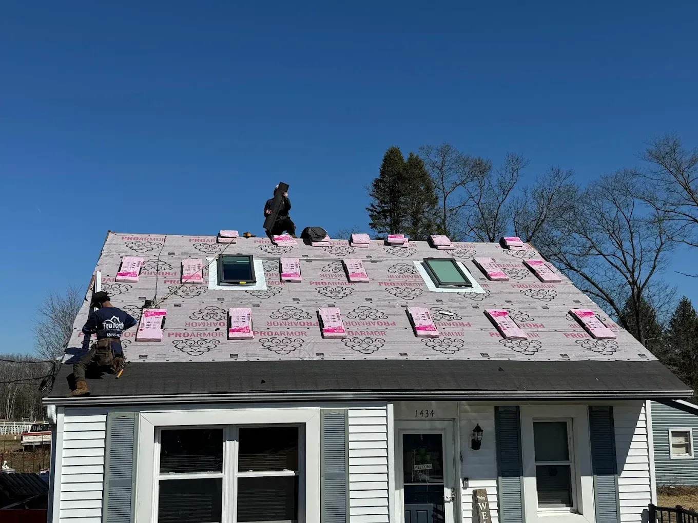 House roof under repair with pink insulation boards and workers on top under a clear blue sky