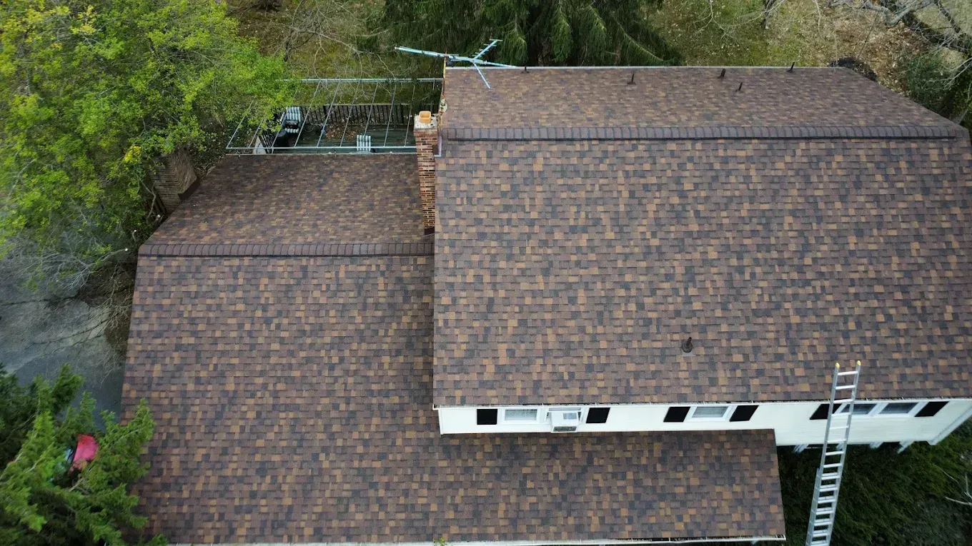 Aerial view of a large brown-shingled house roof surrounded by trees