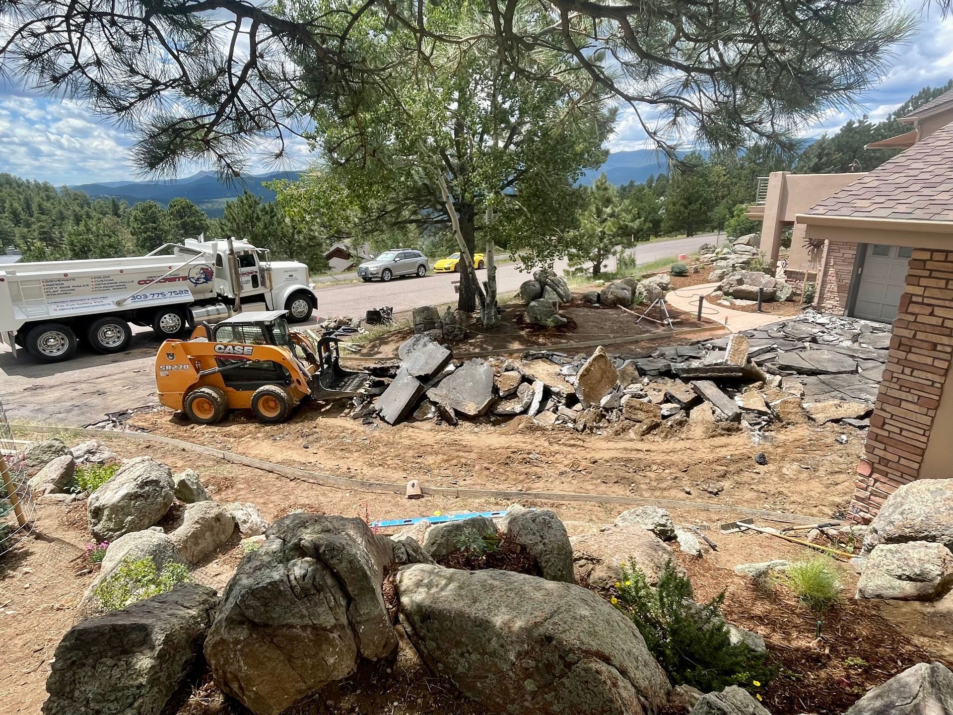 A dump truck is driving down a dirt road next to a house.