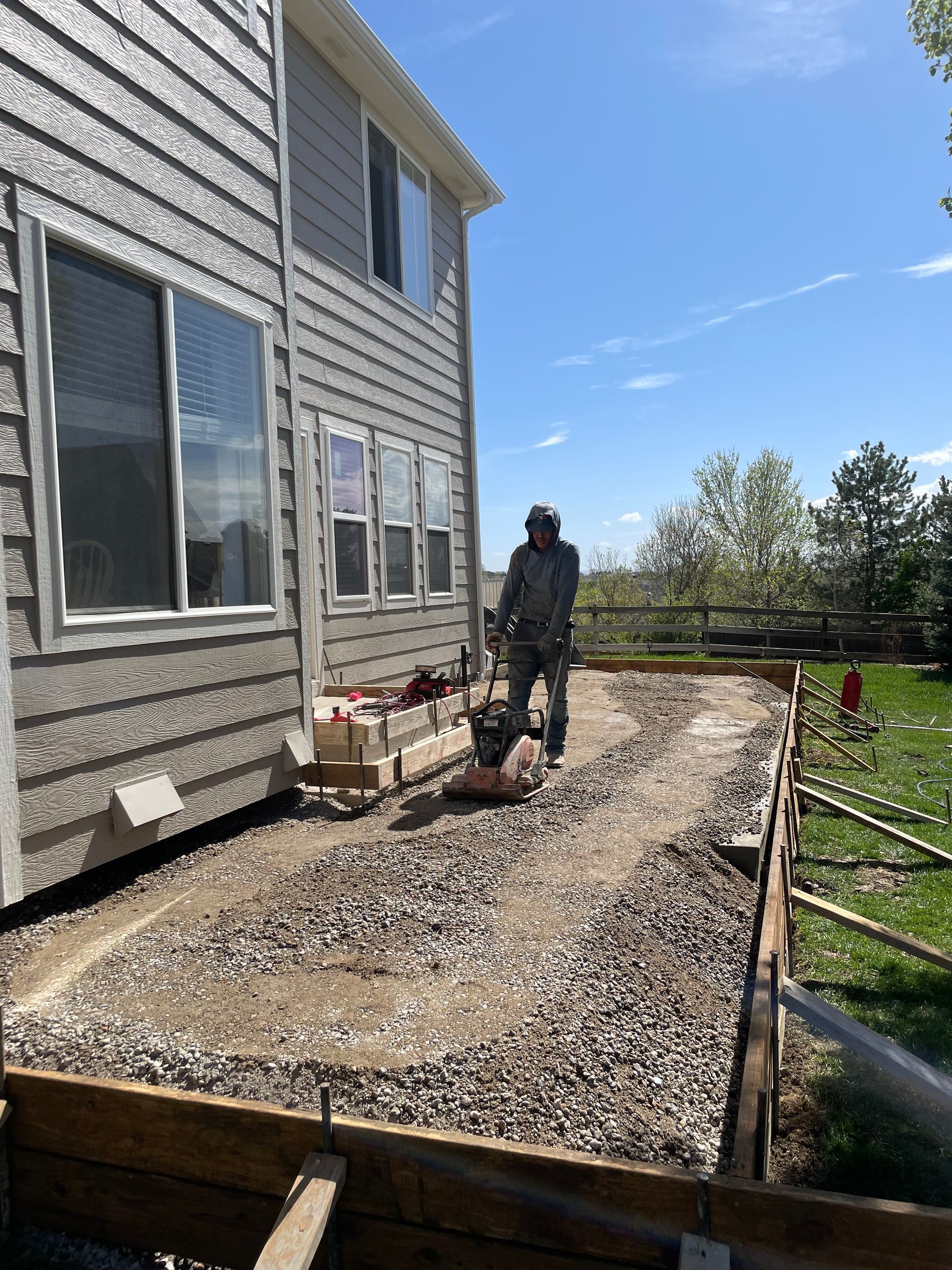 A man is standing on a dirt road in front of a house.