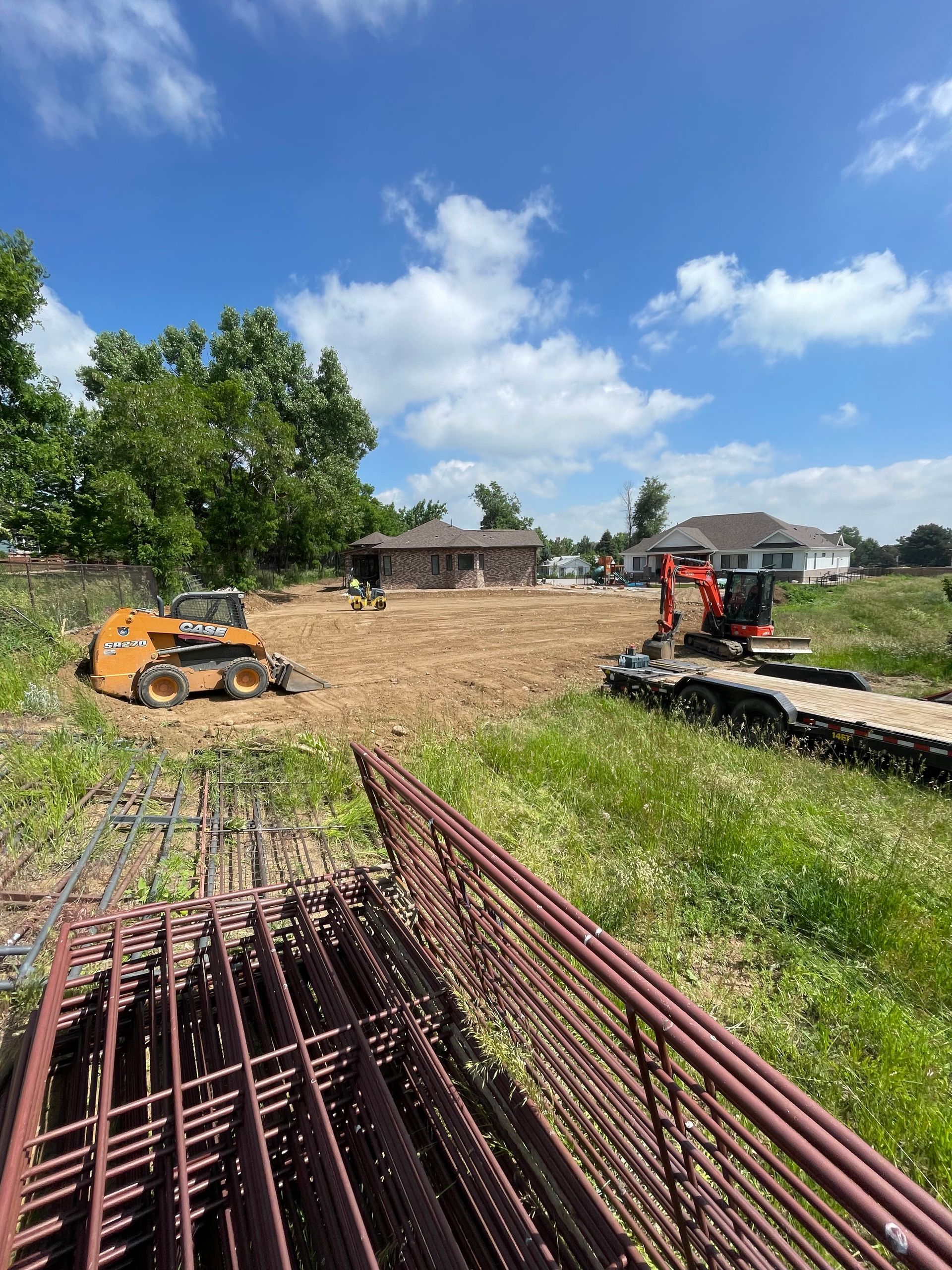 A construction site with a house in the background and a fence in the foreground.